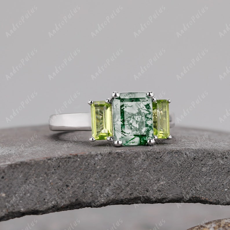 May include: A silver ring featuring a green moss agate centre stone with two smaller green stones flanking it.