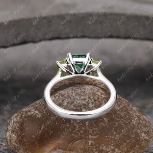 May include: A silver ring set with three green gemstones. The centre stone is a larger emerald cut stone, and the two side stones are smaller pear-shaped stones.