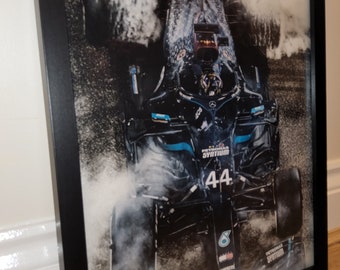 May include: A black Formula 1 race car with the number 44 on the side, driving through a puddle of water, creating a spray of water droplets. The car is covered in a layer of water droplets and the background is blurred.