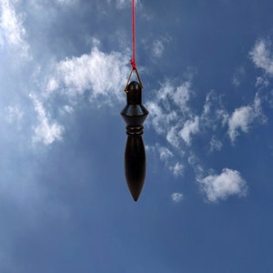 Op de afbeelding: Een zwarte slinger hangt aan een rood touwtje tegen een blauwe lucht met witte wolken.