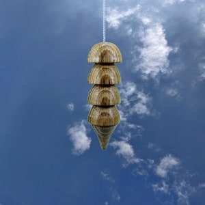 Op de afbeelding: Een houten slinger met vier lagen die hangt aan een wit touw tegen een blauwe lucht met witte wolken.