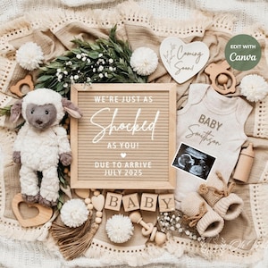 May include: A neutral gender baby announcement with a white letter board that reads "We're just as shocked as you! Due to arrive July 2025". The letter board is surrounded by a variety of baby items, including a stuffed lamb, a wooden heart with the text "Coming Soon", a baby onesie with the text "Baby Smithson", a wooden rattle, and a wooden block that reads "Baby".