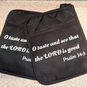 Puede incluir: Dos manoplas de horno negras con texto blanco. El texto dice "Oh, prueba y ve que Jehová es bueno, Salmo 34:8".