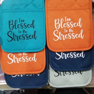 May include: Set of four pot holders with the phrase "Too Blessed To Be Stressed" in white and black lettering on a teal, orange, navy blue, and gray background.