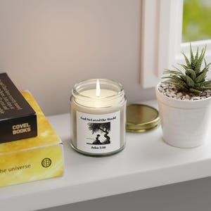 Puede incluir: Un tarro de vidrio para velas con una etiqueta blanca que dice "God So Loved the World" y "John 3:16". La etiqueta presenta una ilustración en blanco y negro de un árbol y una persona sentada debajo.