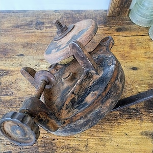 May include: A vintage, rusty, cast iron hand-crank sharpening tool with a round grinding wheel. The tool has a wooden handle and a metal crank.