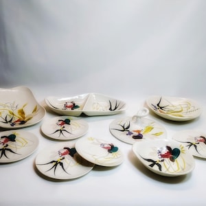 May include: A set of 10 white ceramic dishes with a floral design. The dishes are in various shapes and sizes, including a divided serving dish, a round serving dish, and several smaller plates. The floral design features black, green, yellow, and red accents.