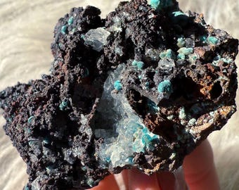 May include: A rough, dark gray rock with embedded blue-green crystals and clear, glassy crystals. The rock has a natural, uneven surface.
