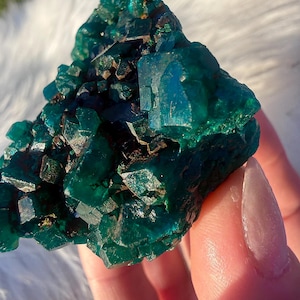 以下が含まれることがあります： 鮮やかなエメラルドグリーンの鉱物標本のクローズアップ。結晶構造は、キラキラと反射する表面を持つ、多数の小さな角張った形状を特徴としています。鉱物は豊かで深い色と、ざらざらとした質感の外観をしています。