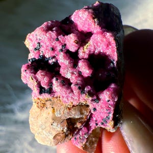 May include: A pink and black crystal cluster with a clear, glassy crystal at the bottom. The crystal cluster is rough and has a natural, organic shape.