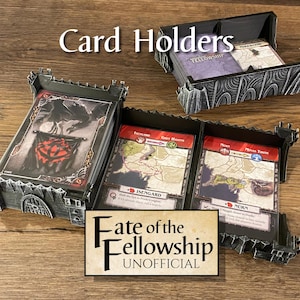 May include: Black card holders with the text "Card Holders" and "Fate of the Fellowship UNOFFICIAL". The holders are filled with game cards featuring maps and illustrations. The holders are designed to look like castle walls.
