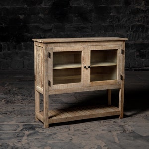Könnte beinhalten: Ein rustikaler Holzschrank mit zwei Glastüren und einem unteren Regal. Der Schrank hat eine abgenutzte Oberfläche und ist aus recyceltem Holz gefertigt.