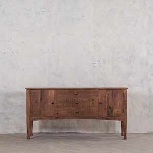 May include: A dark brown wooden sideboard with three drawers and two doors. The sideboard has a curved front and sits on four legs.