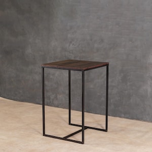 May include: A square side table with a dark wood top and a black metal frame. The table has a minimalist design. The table is approximately 61 cm tall and 46 cm wide.