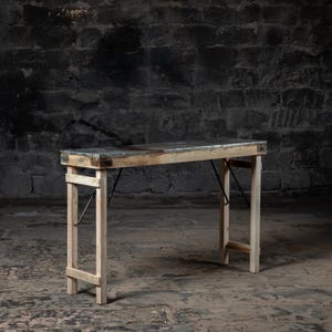 May include: A rustic wooden folding table with a distressed metal top. The table has a simple design with two legs on each side and a rectangular top. The table is made of natural wood and has a weathered look.