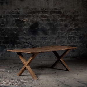 May include: A rustic wooden table with a rectangular top and an X-shaped base. The table is made of dark brown wood and has a distressed finish.