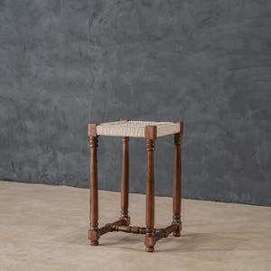 May include: A wooden stool with a woven cane seat. The stool has four legs and a simple design.