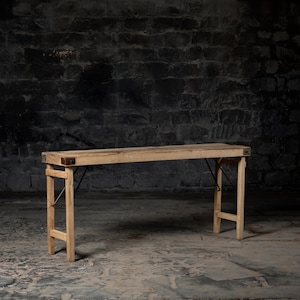 May include: A rustic wooden folding table with a natural wood finish. The table has a simple design with a rectangular top and two folding legs. The table is made of solid wood and has a distressed look.