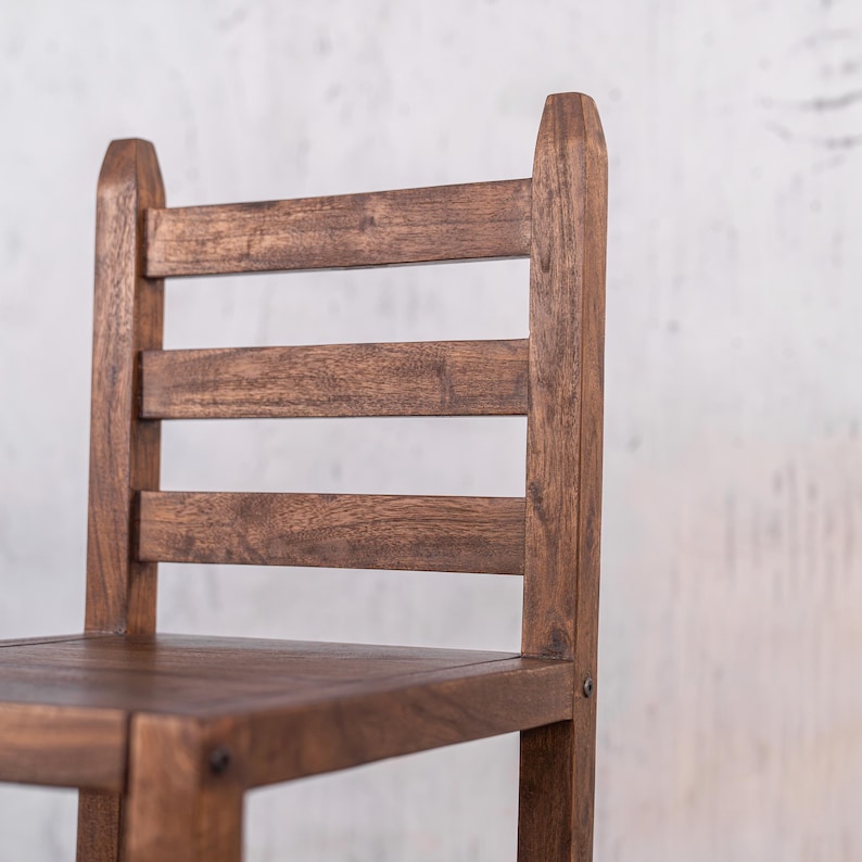 Puede incluir: Primer plano de una silla de madera con dise&ntilde;o de respaldo de escalera. La silla es de madera marr&oacute;n oscuro y presenta un asiento y tres listones horizontales para el respaldo. La silla tiene una est&eacute;tica simple y r&uacute;stica.