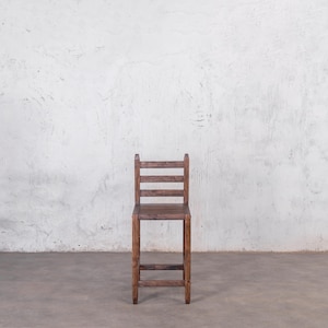 Puede incluir: Un taburete alto de madera oscura con respaldo de escalera. El taburete tiene una construcci&oacute;n sencilla y robusta. El asiento es cuadrado y el respaldo tiene tres listones horizontales. Altura aproximada de 76 cm.
