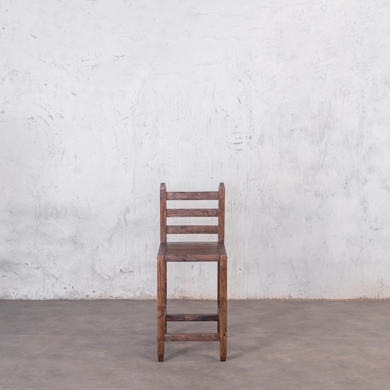 Puede incluir: Un taburete alto de madera oscura con respaldo de escalera. El taburete tiene una construcci&oacute;n sencilla y robusta. El asiento es cuadrado y el respaldo tiene tres listones horizontales. Altura aproximada de 76 cm.