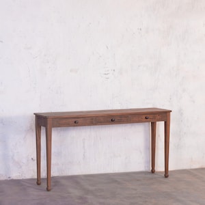 Op de afbeelding: Een lange, houten consoletafel met drie laden en gedraaide poten. De tafel is bruin en heeft een verweerde afwerking.