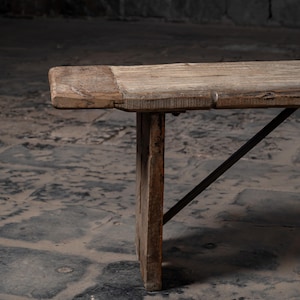 May include: A rustic wooden bench with a simple design. The bench has a natural wood finish and is supported by two sturdy legs and a metal brace.