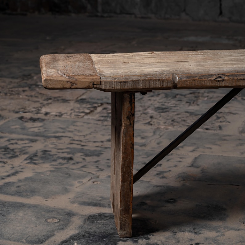 May include: A rustic wooden bench with a simple design. The bench has a natural wood finish and is supported by two sturdy legs and a metal brace.