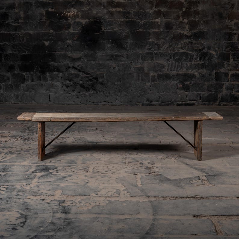 May include: A rustic wooden bench with a weathered finish and metal supports. The bench is made of reclaimed wood and has a natural, distressed look.
