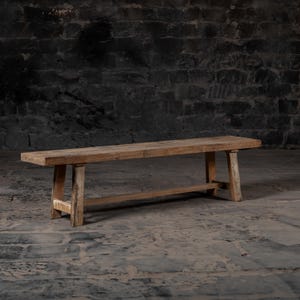 May include: A long, rustic wooden bench with a natural finish. The bench has a simple design with four legs and a rectangular top. The bench is made of reclaimed wood and has a weathered look.