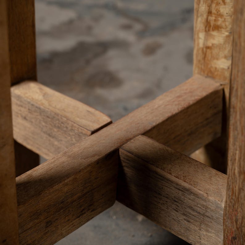 May include: Close-up of the wooden base of a table or stool. The base is made of four pieces of wood that are joined together in a cross shape. The wood is a light brown colour and has a natural finish.