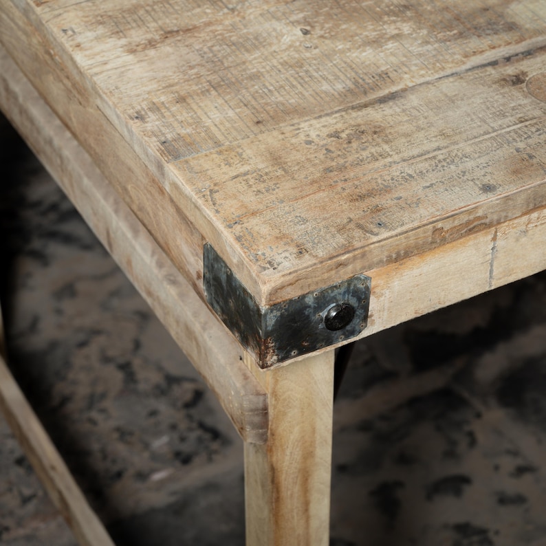 May include: Close-up of a wooden table corner with a metal bracket. The table has a light wood finish and the bracket is black.