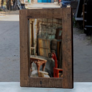Peut inclure: Un cadre en bois rustique avec un miroir à l'intérieur. Le cadre est brun foncé et a une finition vieillie. Le miroir reflète une image floue d'une pièce avec des meubles.