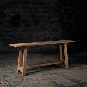 May include: A light brown wooden console table. It features a rectangular top and angled legs, with a connecting bar for stability. The table's design is minimalist, showcasing the natural wood grain. Ideal for hallways or living spaces.
