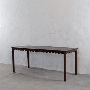 Peut inclure: Une table en bois brun foncé avec un bord festonné. La table a quatre pieds droits et est placée contre un mur blanc. La table mesure environ 183 cm de long.