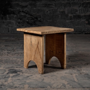 Peut inclure: Un tabouret en bois rustique avec un plateau rectangulaire et des pieds cintrés. Le tabouret est en bois naturel avec une finition brun clair.