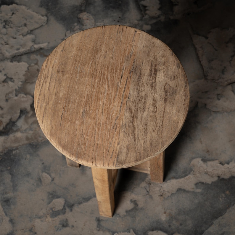 May include: A round wooden stool with a natural wood finish. The stool has a simple design with a circular seat and three legs.