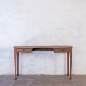 Könnte beinhalten: Ein Holzschreibtisch mit zwei Schubladen auf jeder Seite und einer Öffnung in der Mitte. Der Schreibtisch hat eine hellbraune Oberfläche und steht auf einem weißen Hintergrund.