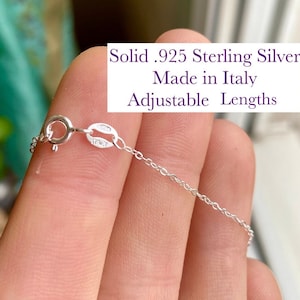 Könnte beinhalten: Eine silberne Kettenkette mit einem Karabinerverschluss. Die Kette ist aus massivem 925er Sterlingsilber gefertigt und in der Länge verstellbar. Der Text "Solid .925 Sterling Silver Made in Italy Adjustable Lengths" ist im Bild sichtbar.