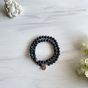 May include: A double-strand bracelet made of dark blue gemstone beads with a silver charm featuring a lotus flower design.