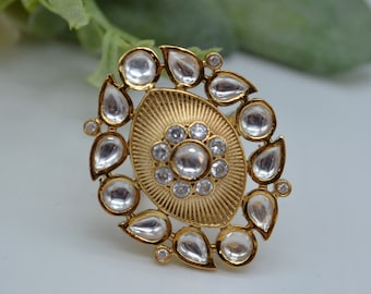 May include: A gold ring with a large, oval-shaped center stone surrounded by smaller, teardrop-shaped stones. The ring is set with clear, sparkling stones.