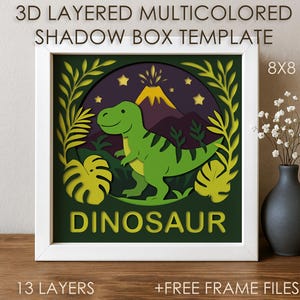 May include: A 3D layered shadow box template with a dinosaur theme. The design features a green dinosaur, volcano, and foliage, framed in a white square. The text "DINOSAUR" is displayed at the bottom. The size is 8x8 inches.