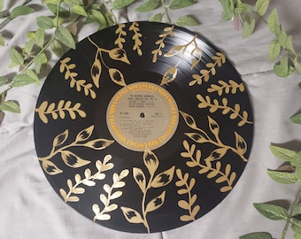 May include: A black vinyl record with a gold leaf design of branches and leaves. The record label is visible and reads "The Mormon Tabernacle Choir's Greatest Hits Vol. II".