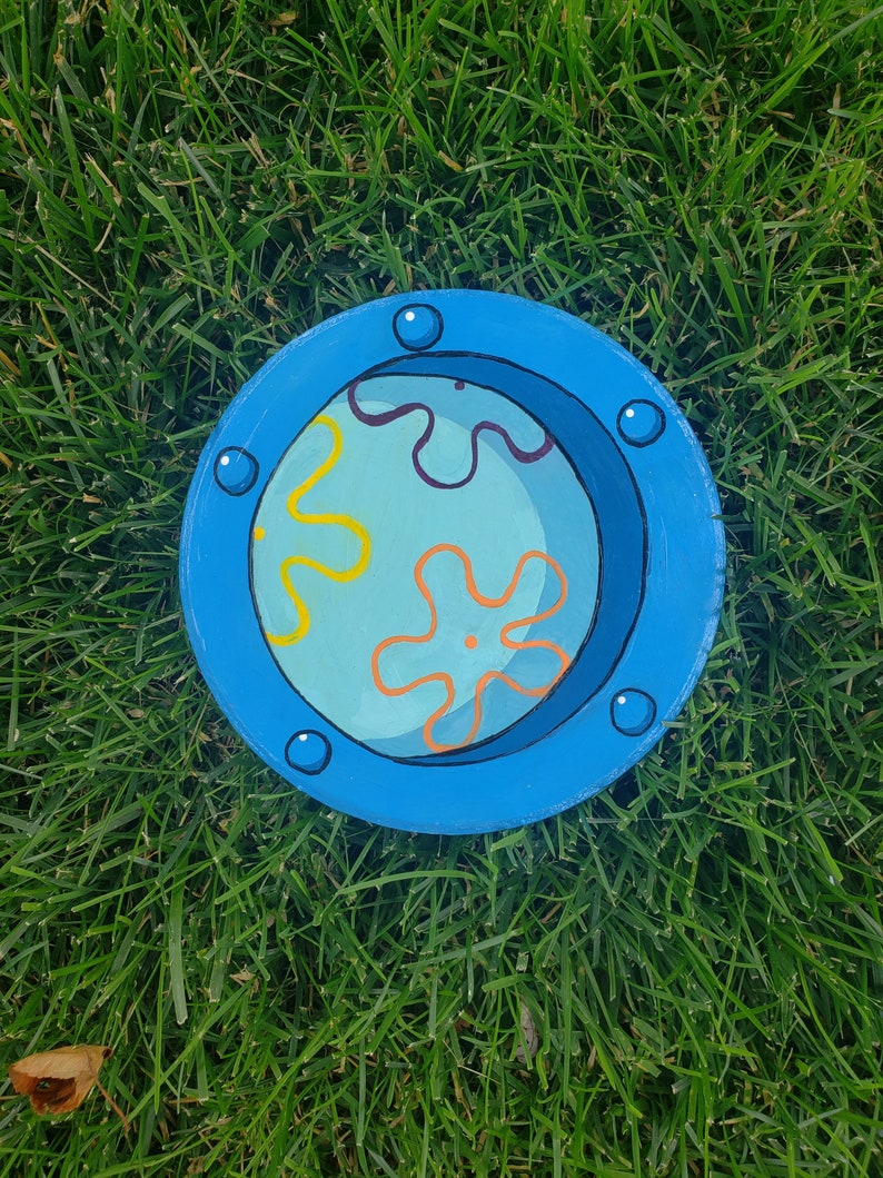 May include: A blue circular dish with a painted design of a yellow and orange flower with a blue background. The dish has a blue rim and five white dots around the rim.