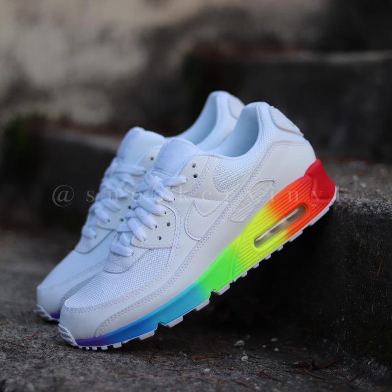 May include: White Nike Air Max 90 trainers with a rainbow gradient on the outsole. The trainers have a white mesh upper and a white swoosh logo.