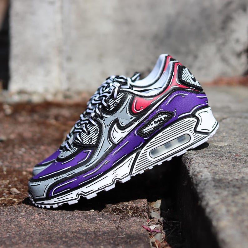 Puede incluir: Un par de zapatillas moradas, grises y blancas con un dise&ntilde;o de contorno &uacute;nico tipo caricatura. Las zapatillas presentan el logotipo de Nike swoosh y las palabras "AIR MAX" en el lateral. Los cordones son negros y blancos.