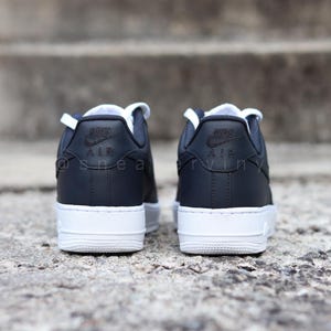 May include: A pair of black leather Nike Air Force 1 sneakers with white soles. The shoes have a black Nike swoosh logo on the side and the word "Air" on the back.