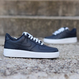 May include: Black leather low-top sneakers with white laces and a white sole. The Nike swoosh logo is visible on the side of the shoe.