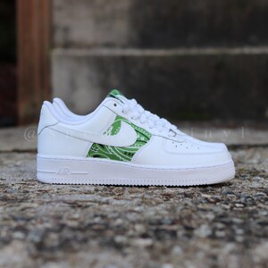 May include: White leather sneaker with green paisley design accents on the side and heel. The shoe features a white sole and laces, with the word "AIR" printed on the side.