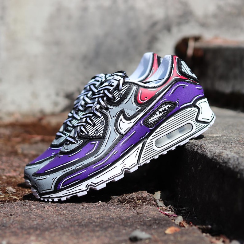 Puede incluir: Par de zapatillas Air Max 90 con un estilo de dibujos animados &uacute;nico. Los zapatos presentan una combinaci&oacute;n de colores p&uacute;rpura y gris con contornos negros, suelas blancas y el logotipo "AIR MAX". Los cordones son blancos y negros.